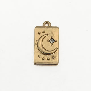 Front side of a gold plated rectangular charm with a crescent moon and clear crystal.