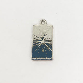 Back side of a silver plated rectangular charm with an engraved starburst pattern.