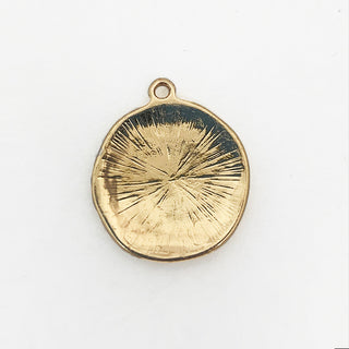 Back of round gold plated charm with engraved starburst pattern.