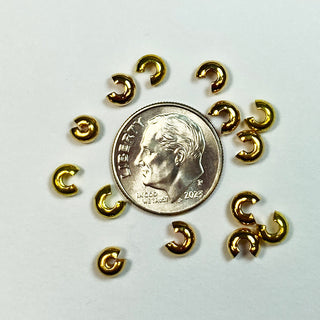 Gold plated bead crimp covers surround a dime for scale.