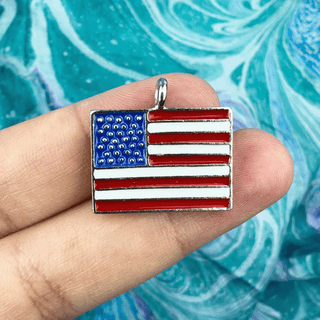 American Flag Charm on a person's fingers on a blue and purple background