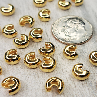 Twenty Four 5mm Gold Plated Crimp Cover Findings next to a Dime for size reference.