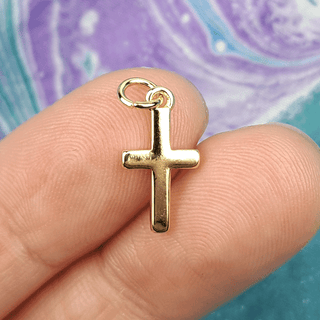 gold cross charm on fingers with multicolor background