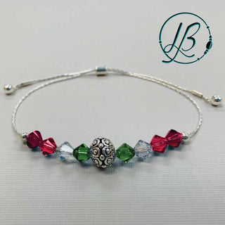 Beginner bracelet kit with silver chain findings, bead, and green, red, clear faceted beads on a grey background