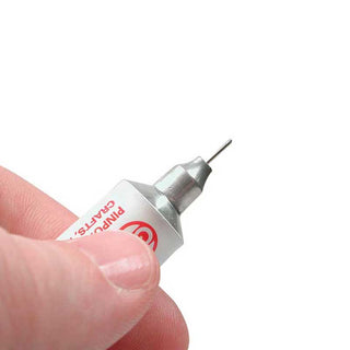 A close-up of a hand holding a small white and silver precision adhesive applicator with a thin metal pin tip against a plain white background.