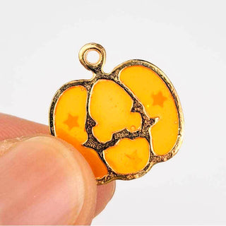 the back side of a Jack O Lantern Charm Enamel Orange Transparent with Gold in a person's fingers