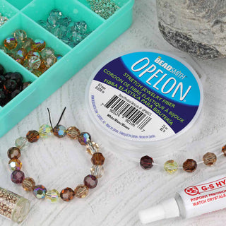 Spool of Opelon Stretch Fiber Cord with beads and tube of glue on a textured surface