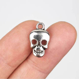 a silver tone skull charm with hollow eyes on a person's fingers