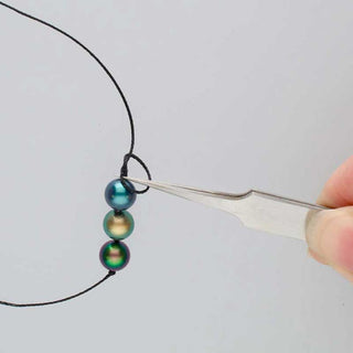Pearl Knotting Tweezers in a person's hand with beads
