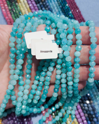 Amazonite Gemstone Beads in a blue / green color on a person's hand over a colorful background