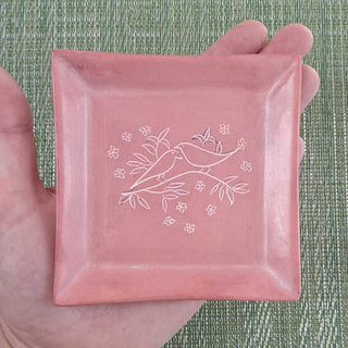 Pink hand carved soapstone tray with birds from Kenya on a person's hand