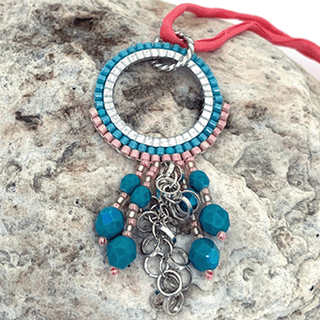 a pink and teal colored pendant on a grey rock