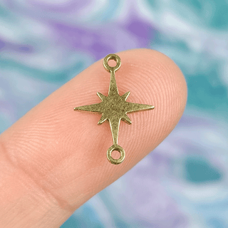 gold north star charm on finger with multicolor background