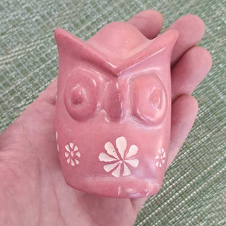 Pink owl-shaped carving held in a hand against a green textured background