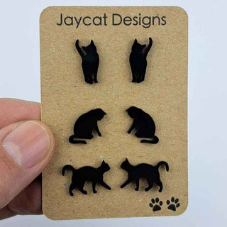 three pairs of black cat stud earrings on a brown paper jewelry card in a person's hand