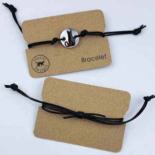 two Black Cat with Heart design black leather bracelet on brown paper jewelry cards on a white background