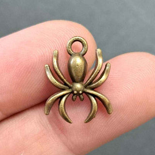 A small antique bronze spider charm held between two human fingers against a dark gray background.