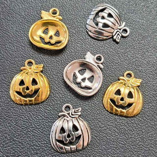 Six pumpkin-shaped jewelry charms in both gold and silver finishes, arranged on a textured dark gray surface.