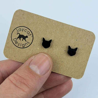 tiny black cat head stud earrings on a brown paper jewelry card in a person's hand