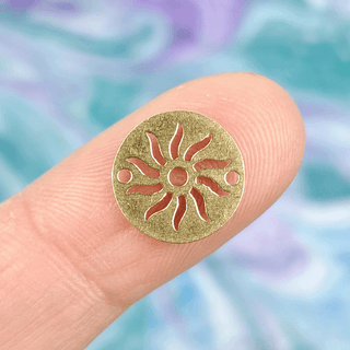 gold sun charm on finger with multicolor background