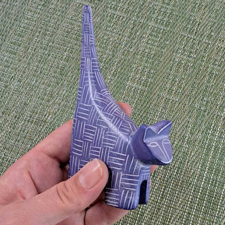 Hand holding a blue/purple geometric-patterned carved cat against a green textured background